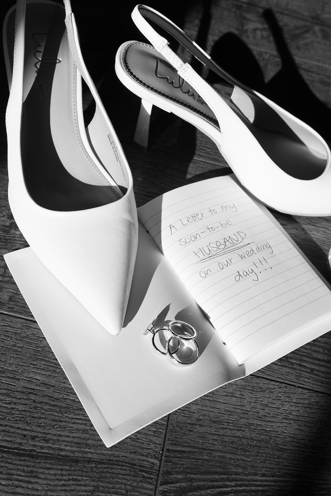 Wedding rings and a heartfelt letter to the groom rest beside the bride’s heels on their romantic wedding morning.
