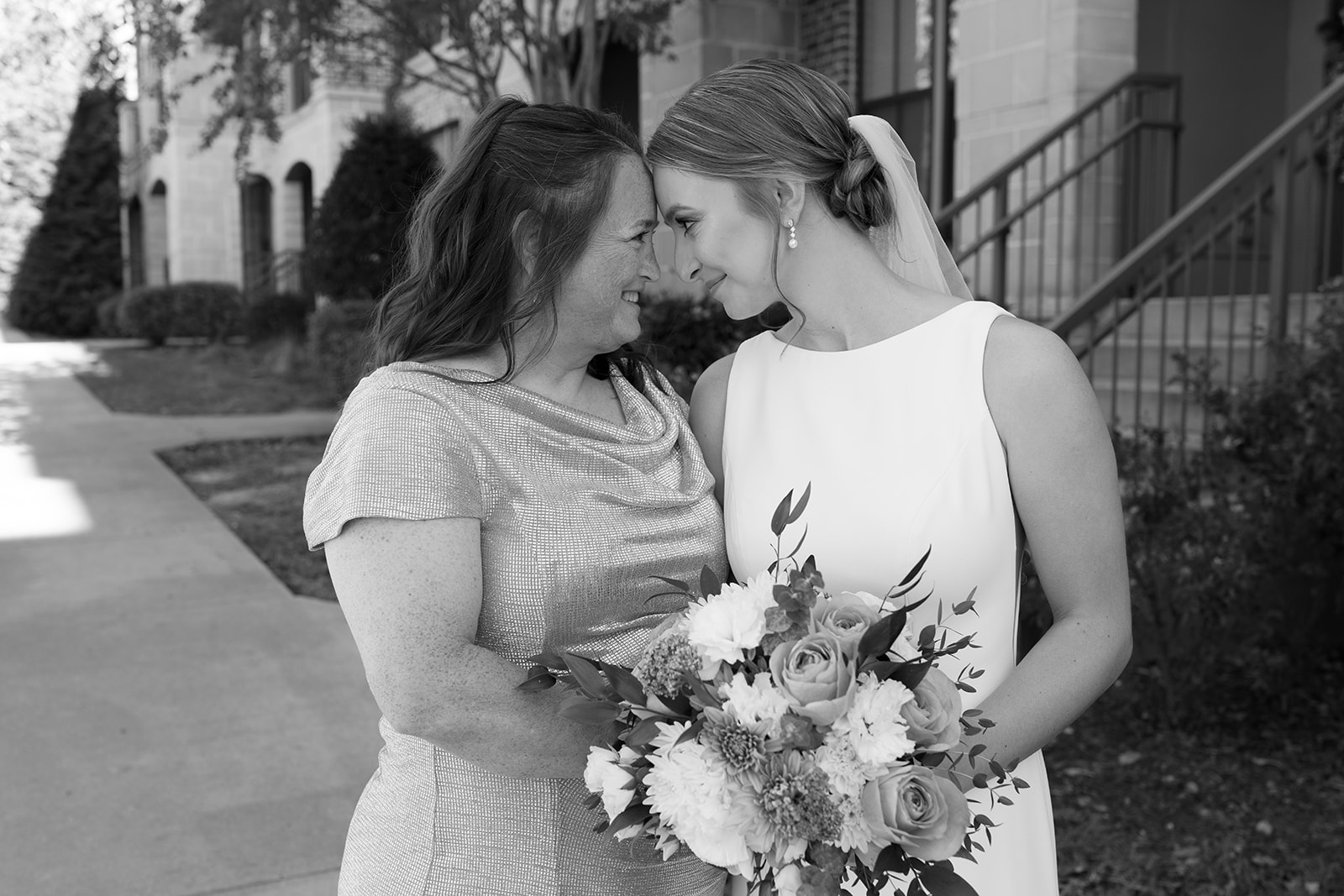 Bride and her mother share a tender moment, smiling with foreheads pressed together.