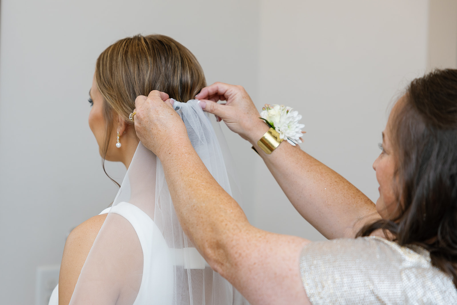 Bride’s mother gently secures a sheer veil as soft light fills the room on the wedding morning at glassy chapel.