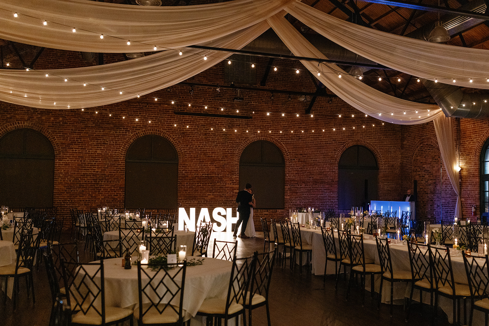 Newlyweds have a private last dance under draped ceilings and glowing lights in the empty reception hall.