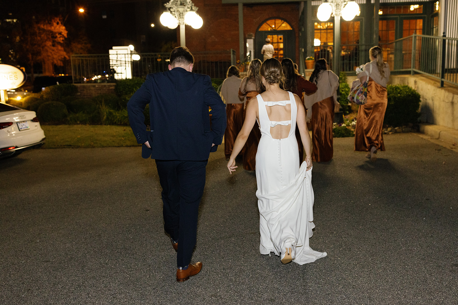 Bride and groom walk toward The L surrounded by bridesmaids in satin rust gowns.