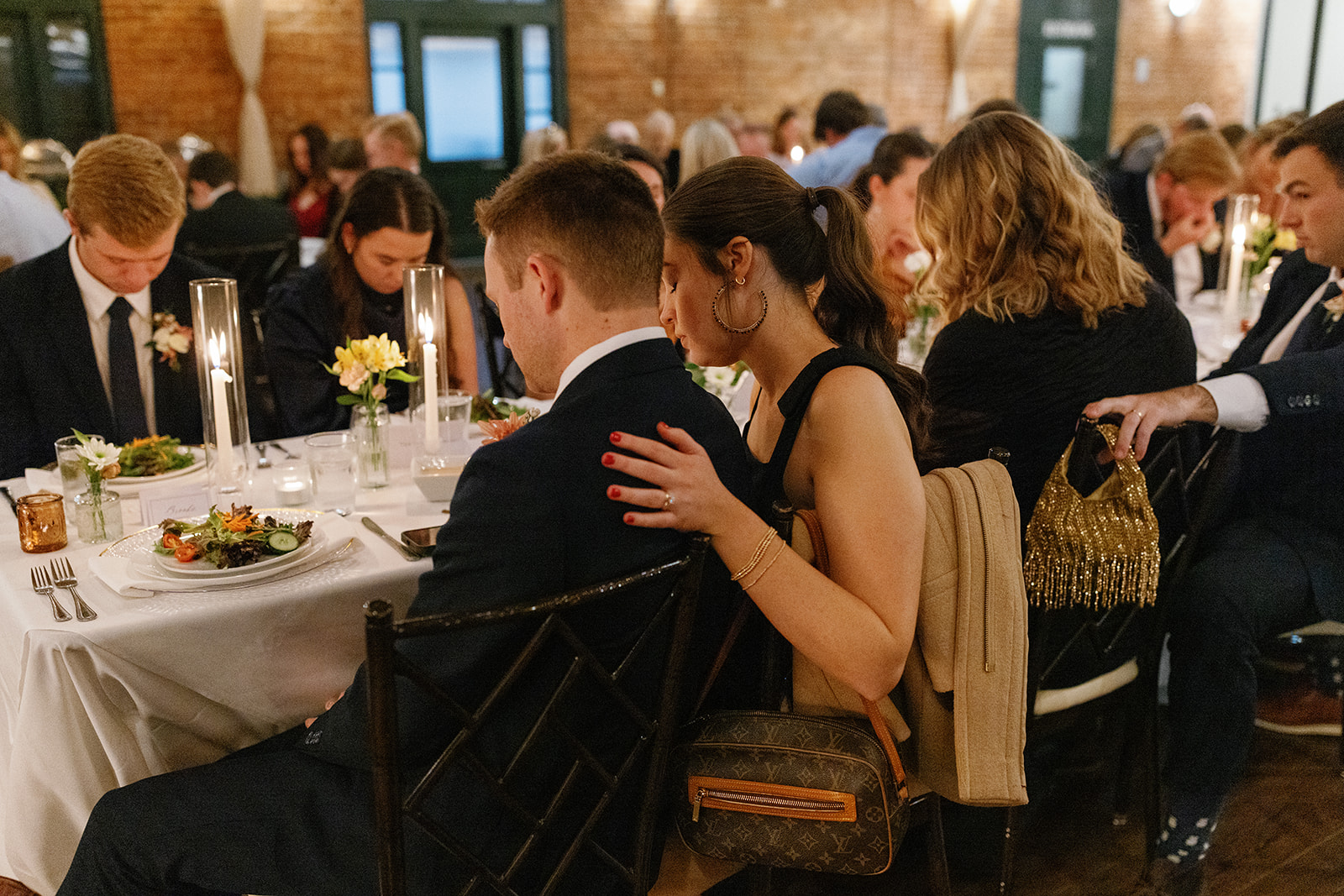 Guests bow their heads in prayer during the reception dinner, surrounded by candlelight.