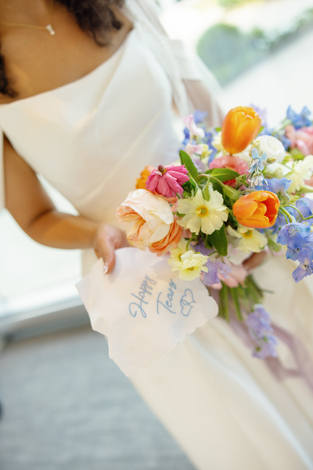 Bride holds a bright spring bouquet and embroidered “Happy Tears” handkerchief before the ceremony.