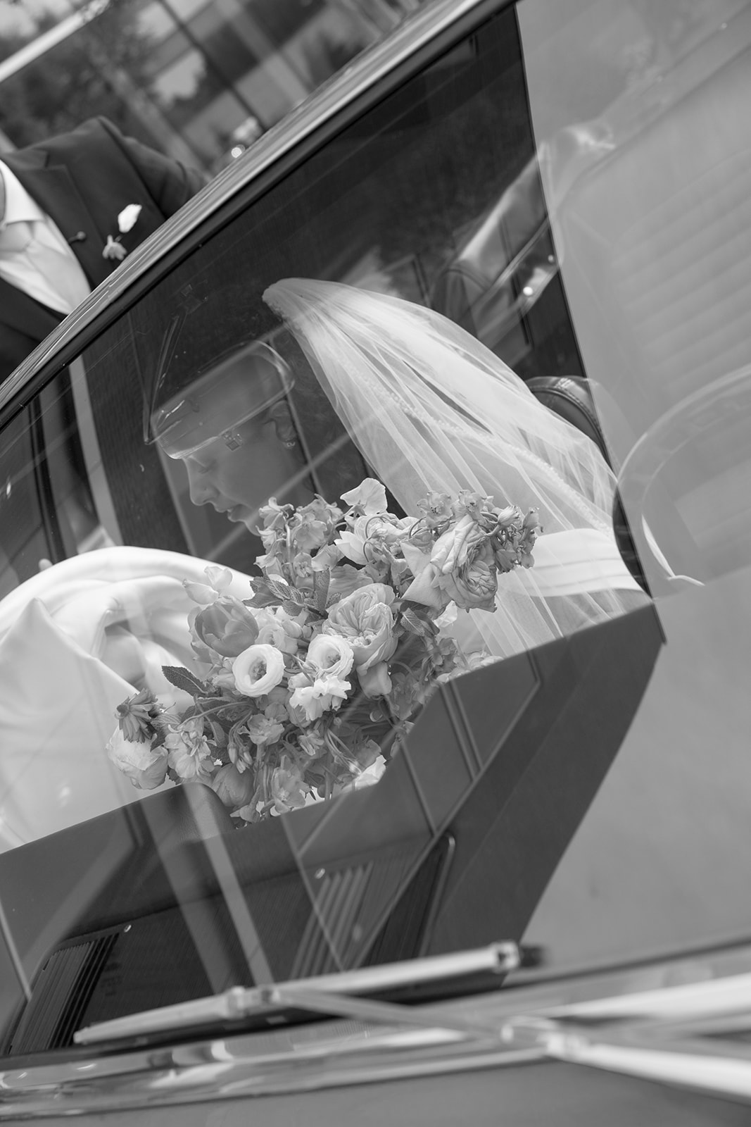 Bride steps into a vintage convertible holding colorful florals as the wedding party looks on outside the venue.