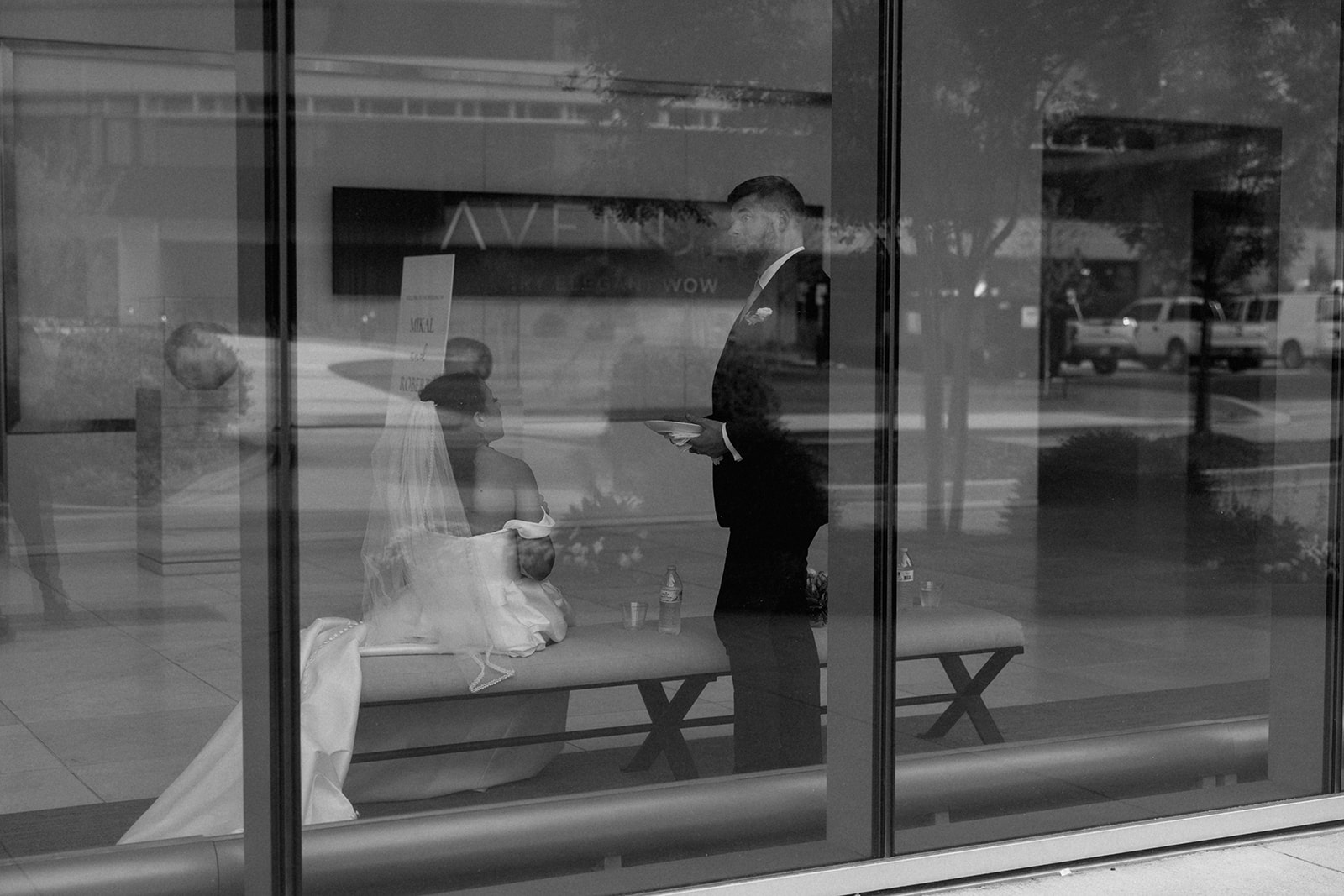 Bride and groom share a quiet, candid moment inside as seen through a large reflective window, taken by a Greenville SC Wedding Photographer.