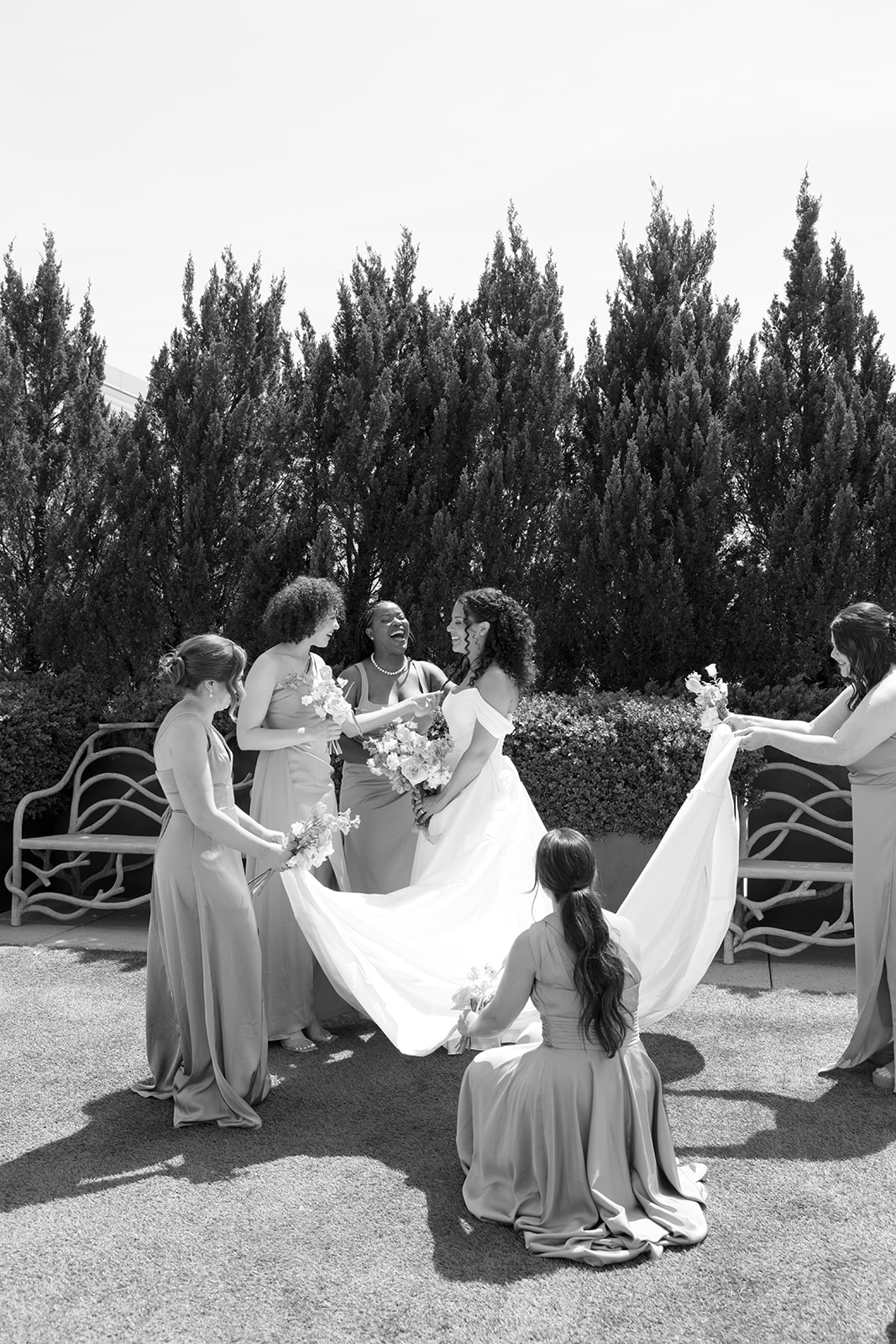 Bridesmaids surround the bride, helping with her train and laughing together before the ceremony, taken by a Greenville SC Wedding Photographer.