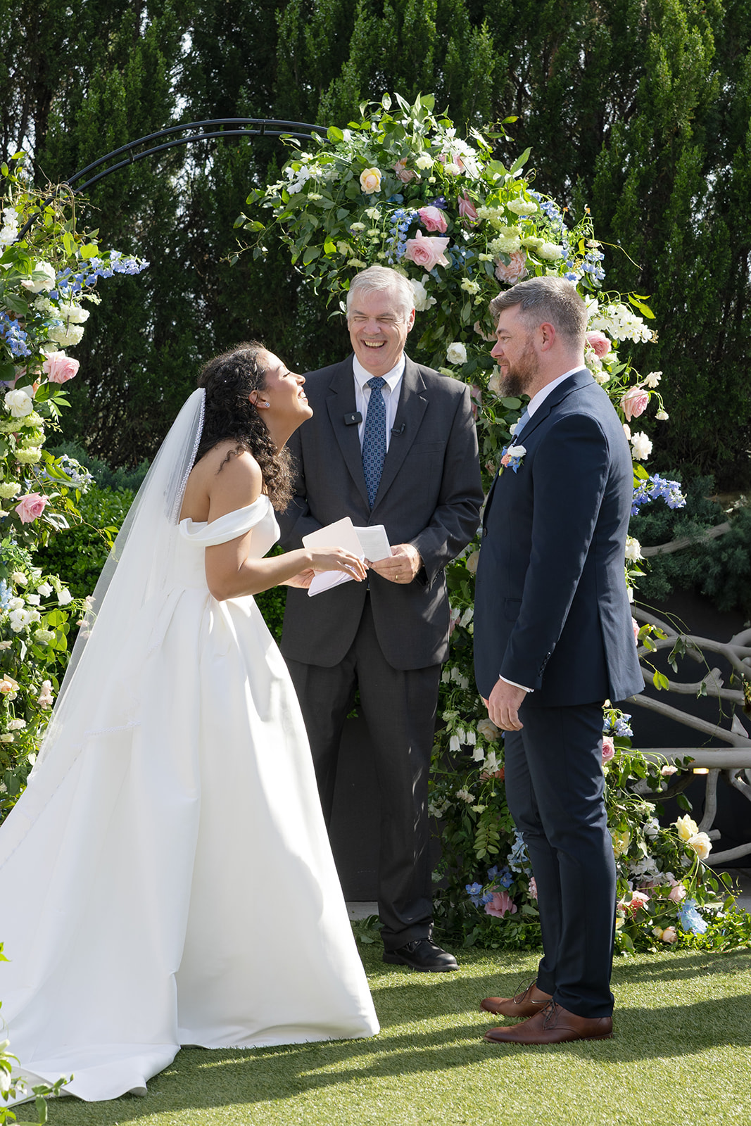 Bride laughs with the groom and officiant during a lighthearted moment at their colorful rooftop ceremony.
