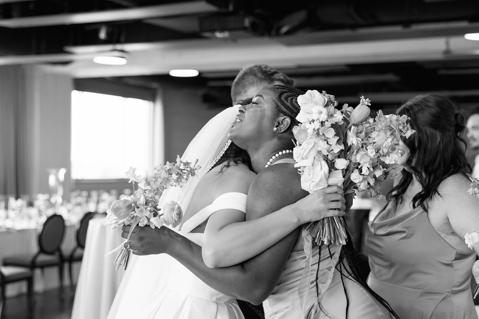 Emotional embrace between the bride and a bridesmaid, both holding colorful spring bouquets, taken by a Greenville SC Wedding Photographer.
