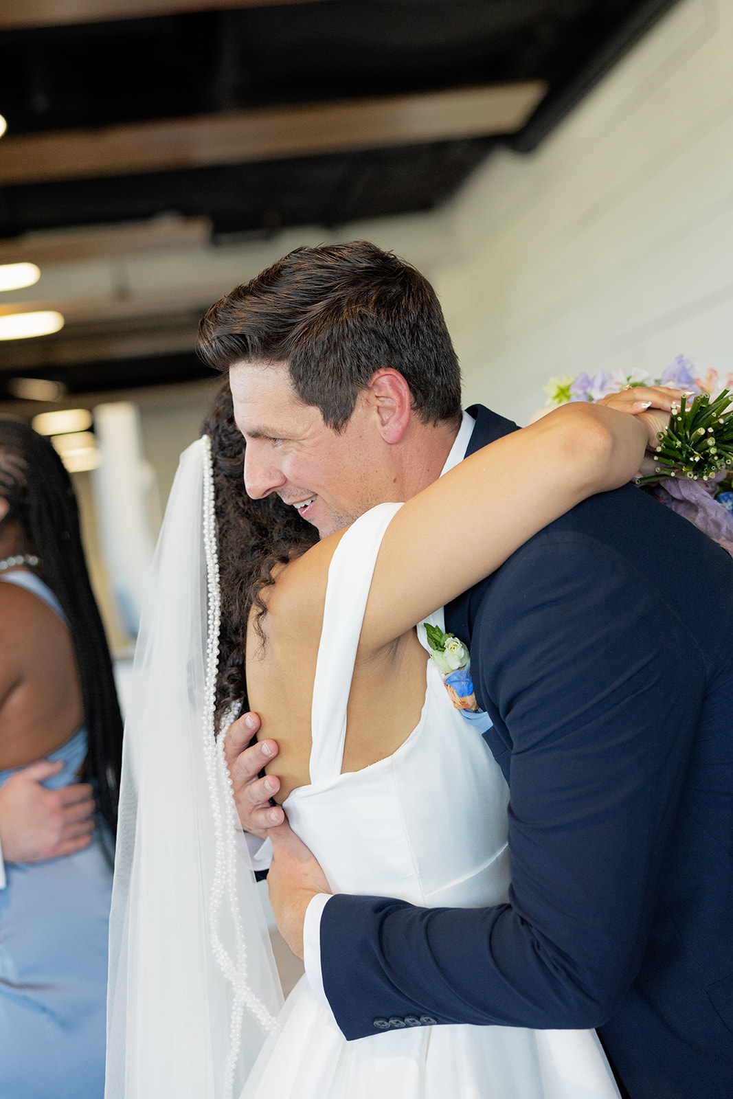 Bride hugs a groomsman tightly, smiling as they celebrate the sweet post-ceremony moments