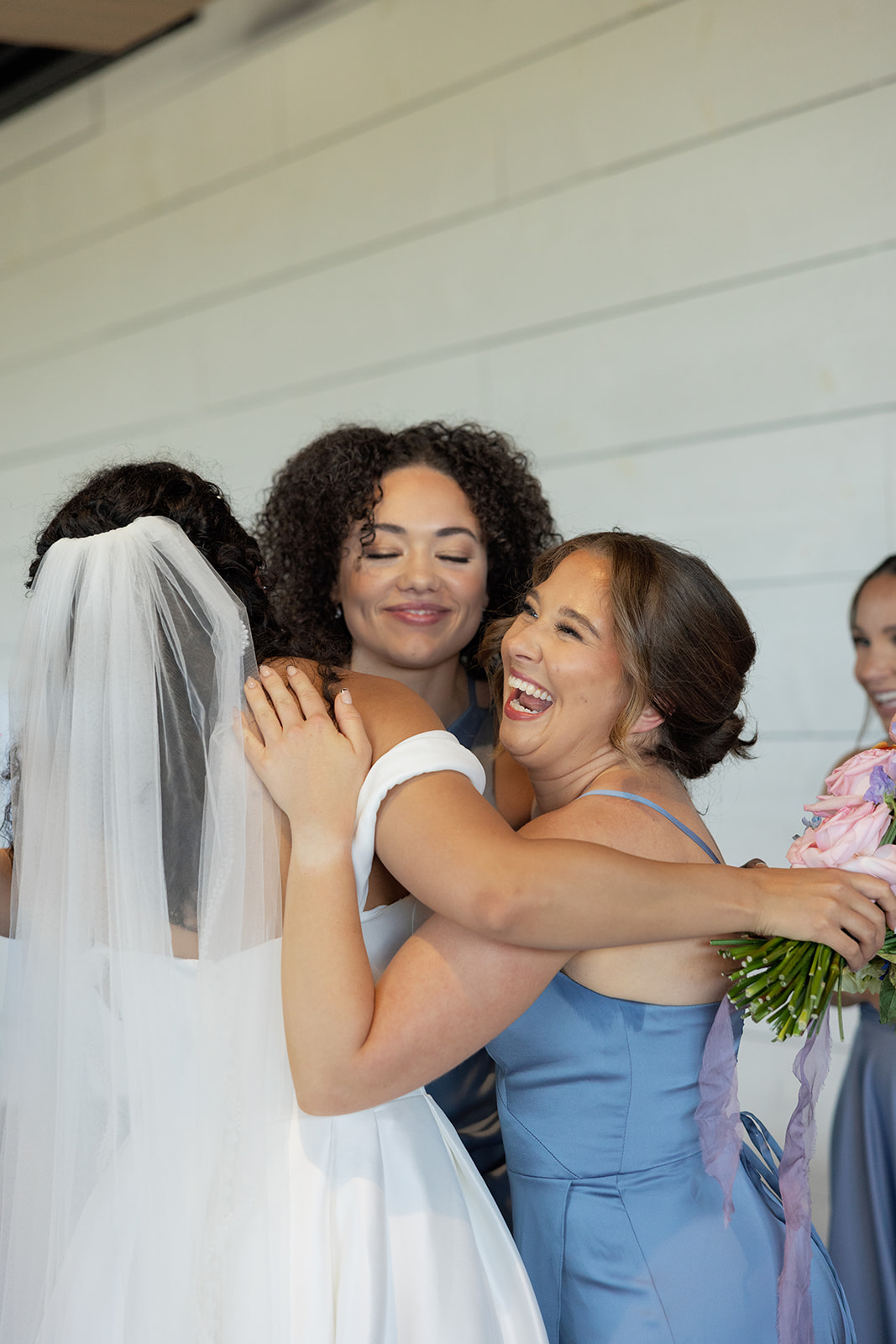 Bride shares a joyful hug with bridesmaids in dusty blue dresses after the ceremony, taken by a Greenville SC Wedding Photographer.