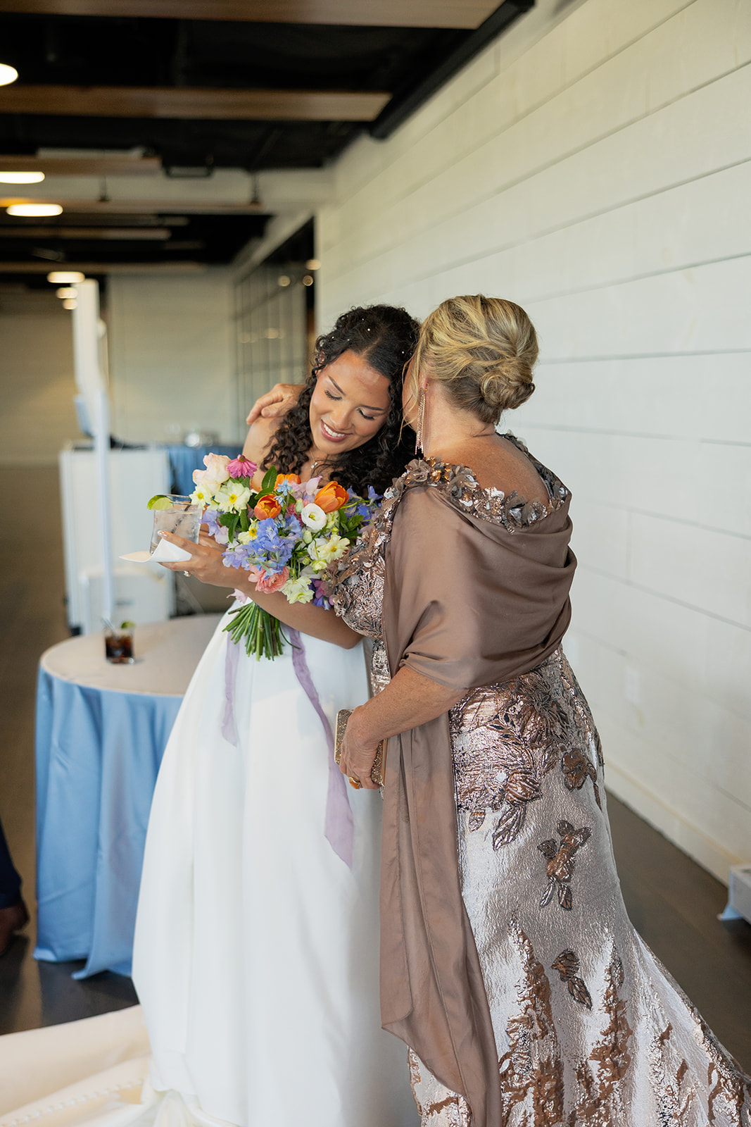 Emotional embrace between the bride and the mother of the bride both holding colorful spring bouquets.