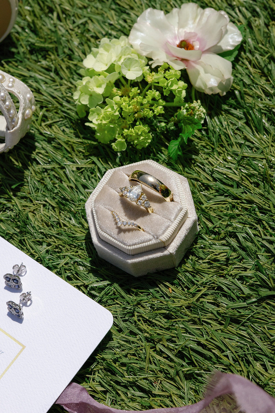 Gold wedding bands and a pear-shaped diamond ring displayed in a velvet ring box with soft florals  taken by a Greenville SC Wedding Photographer..