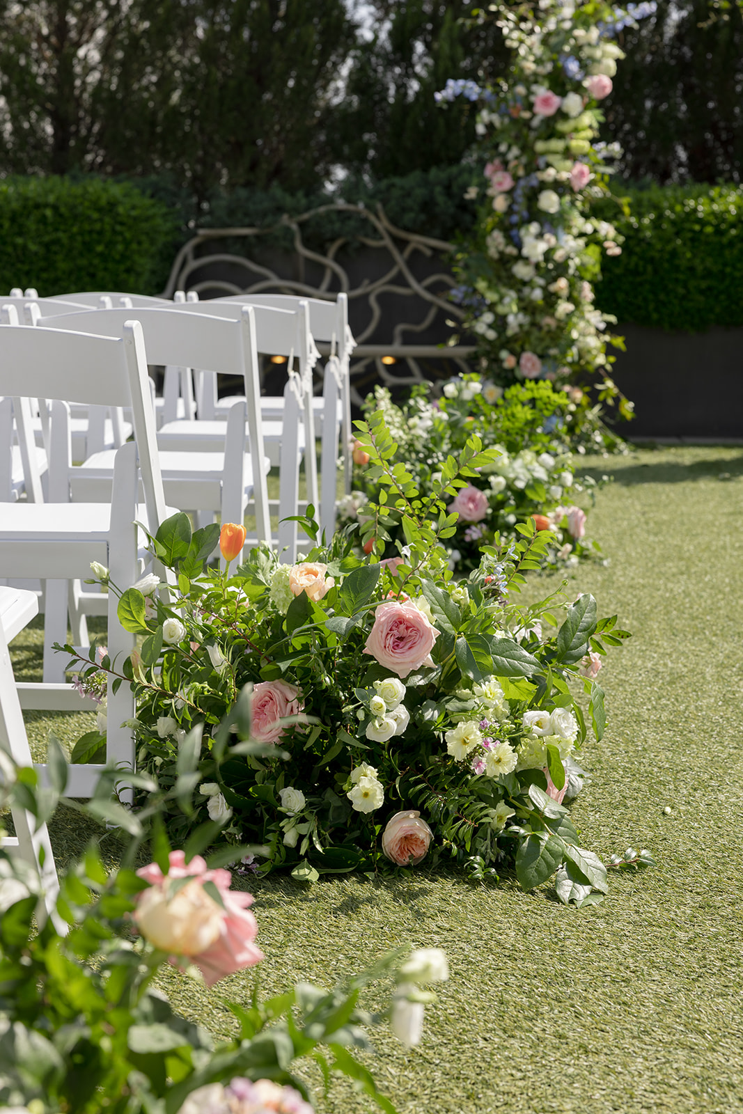 Pastel flower arrangements line white ceremony chairs at an outdoor wedding at Avenue in Greenville, SC.