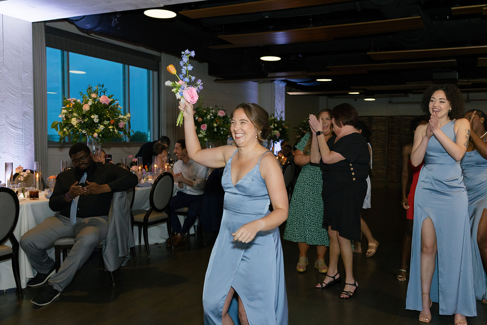 Bridesmaid celebrates catching the bouquet, surrounded by cheering guests.