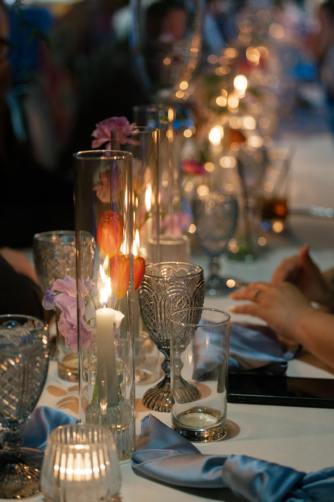 Candlelit reception table with guests enjoying dessert beside pastel blooms and glass votives.
