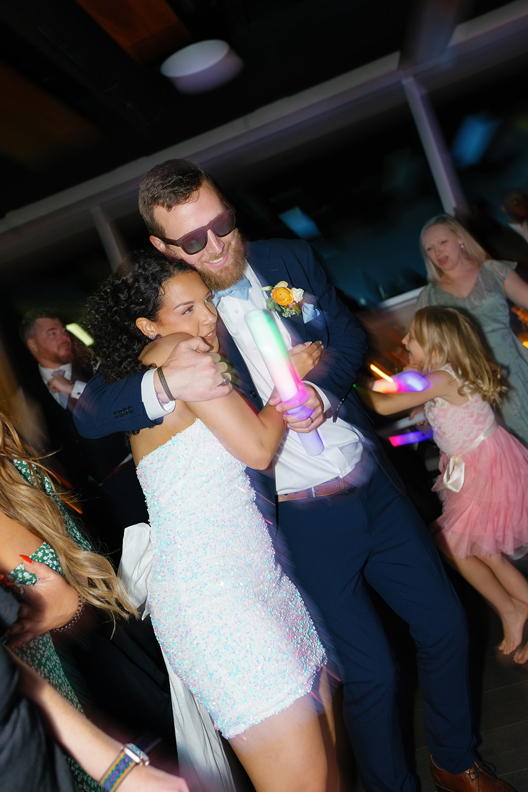 Bride hugs a groomsman on the dance floor while holding glow sticks during the evening celebration.