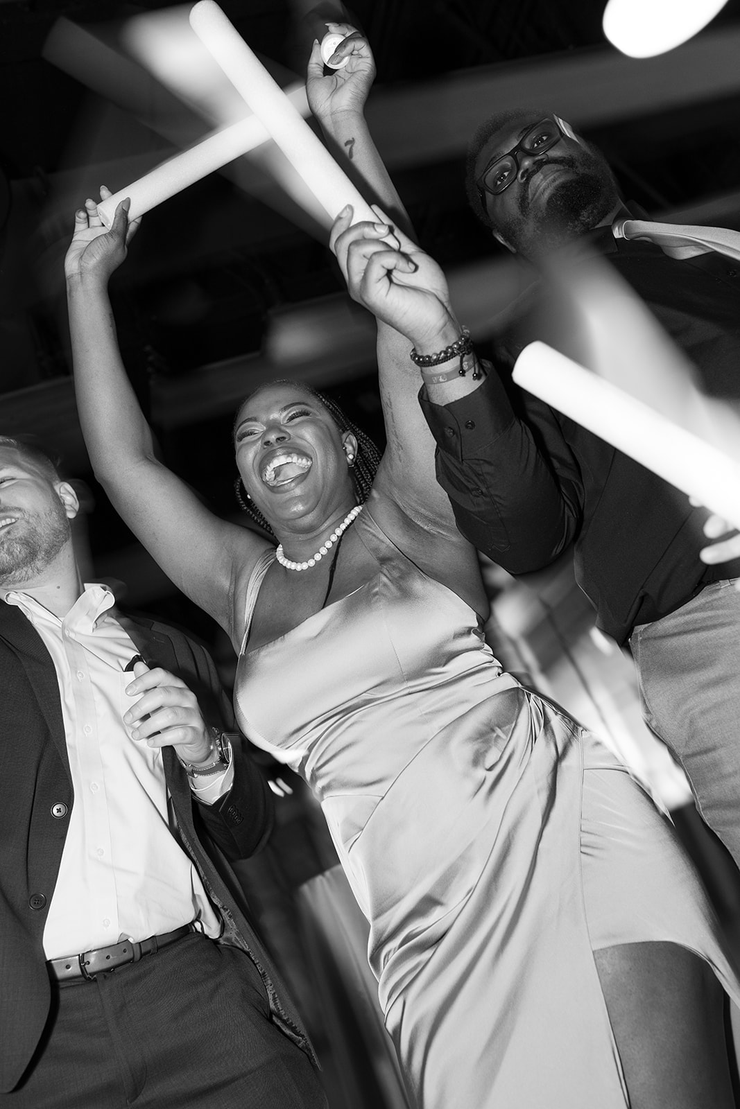 Bridesmaid laughs with arms raised, dancing with friends during the lively wedding reception.