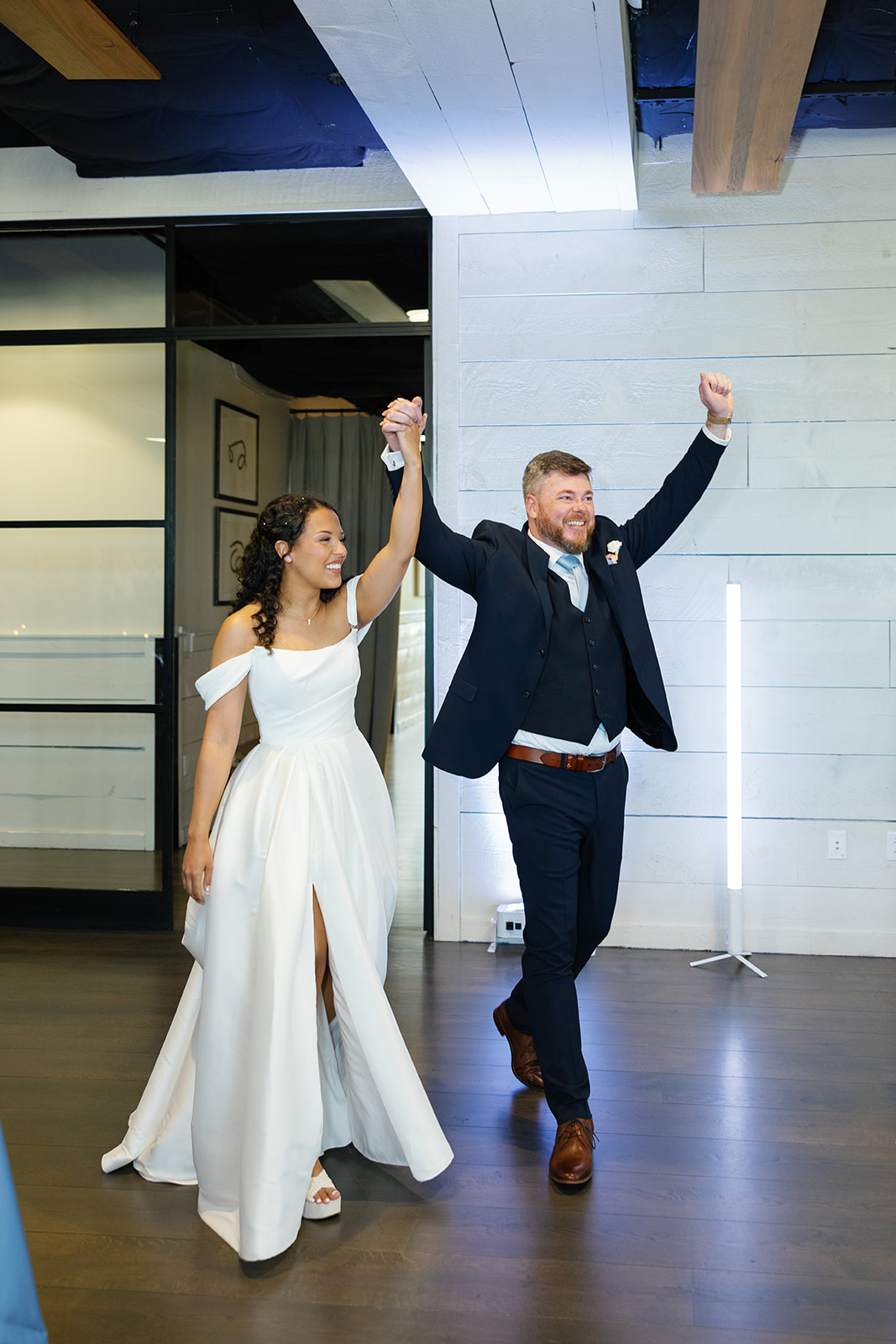Newlyweds make a joyful entrance into their reception, hands raised in celebration, taken by a Greenville SC Wedding Photographer.