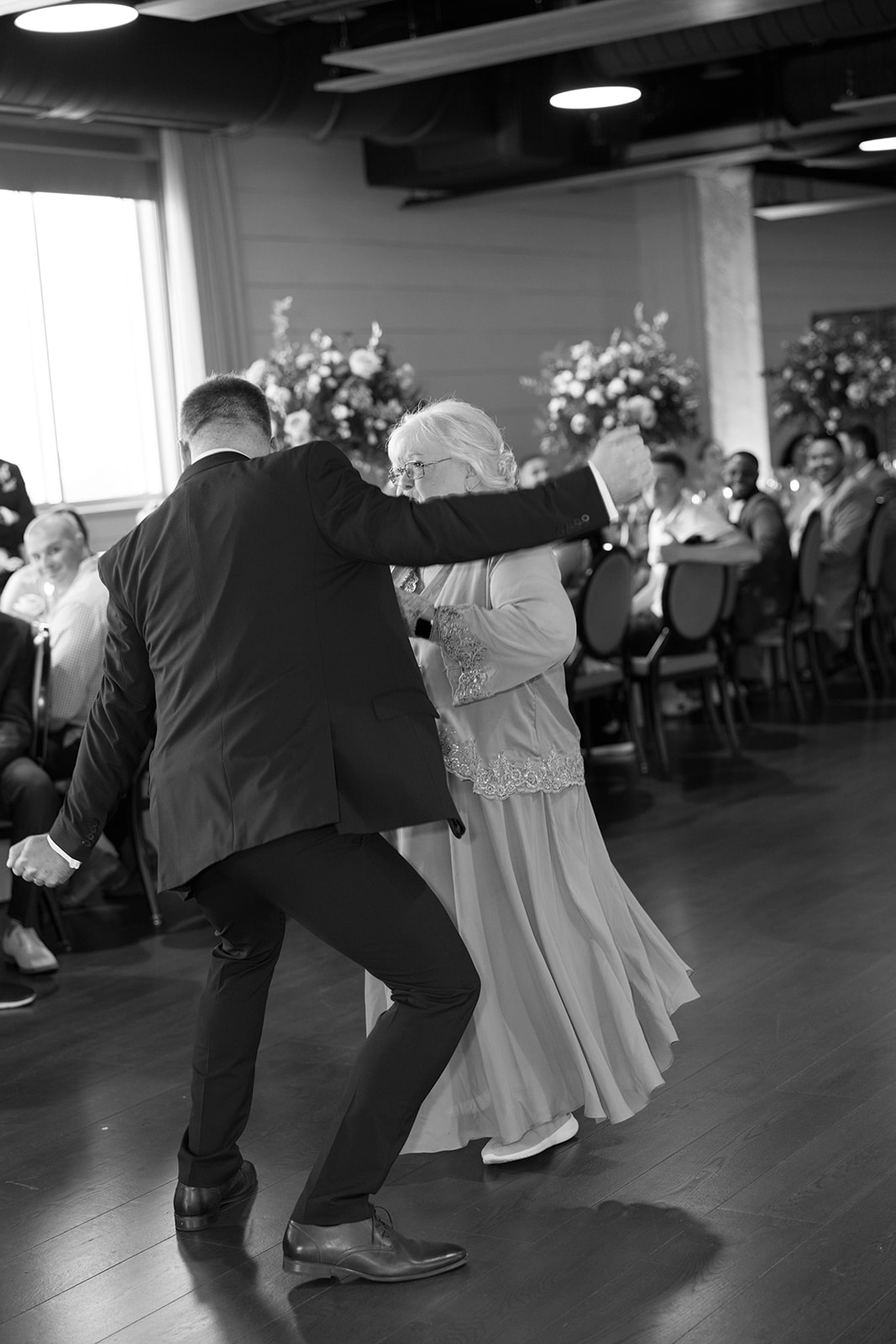 Groom dances playfully with his mother at the reception surrounded by guests.