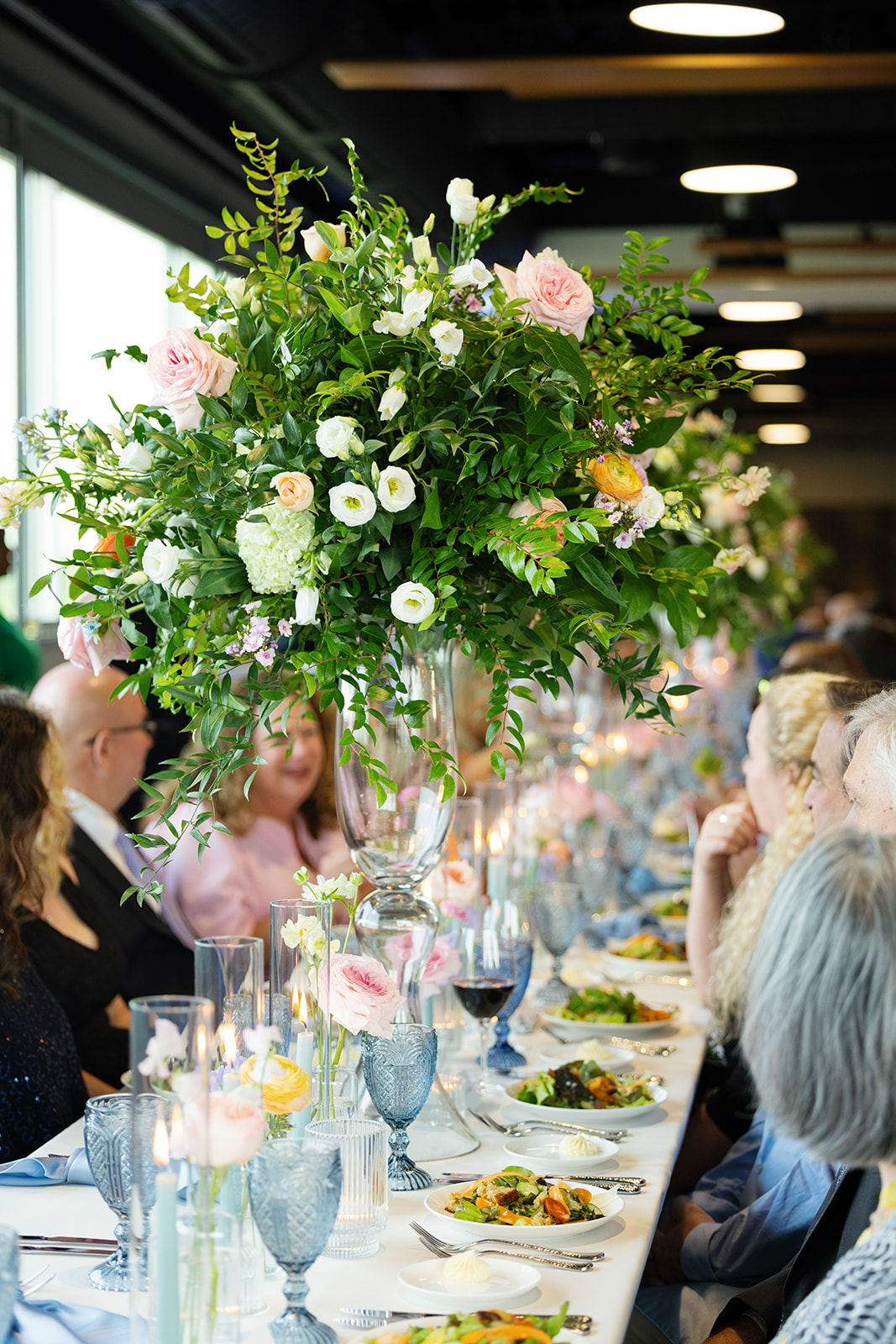 Elegant floral centerpieces and candlelight line a long reception table as guests enjoy dinner.