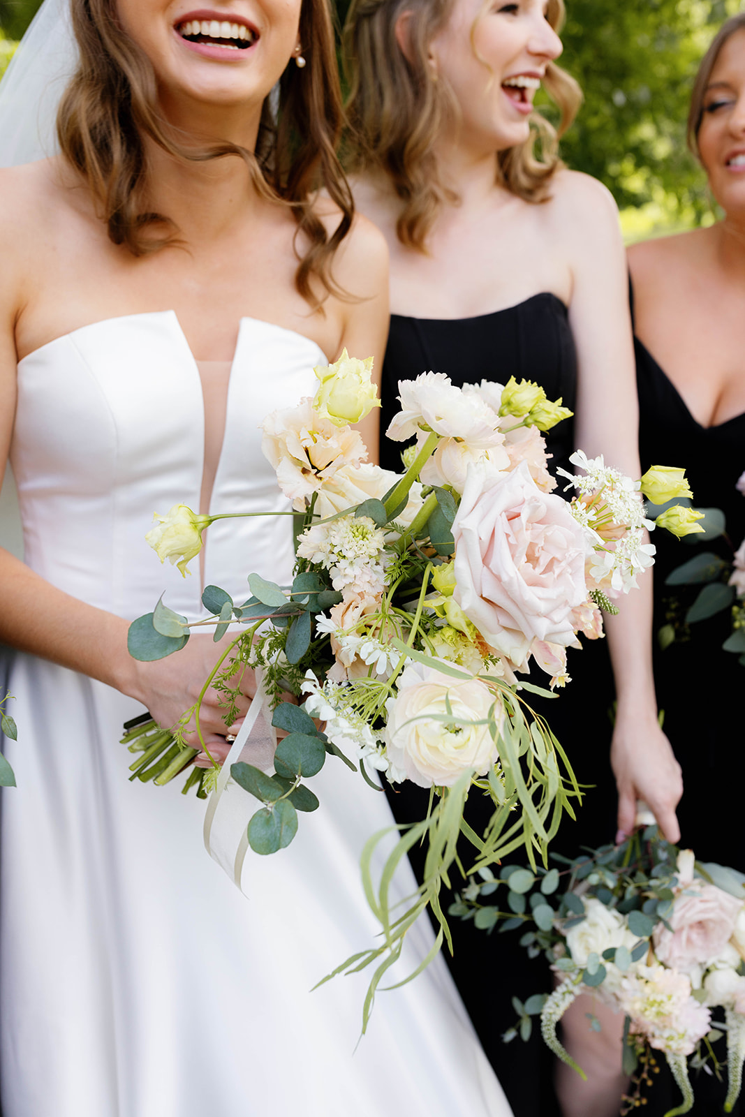 Close-up of pastel garden bouquet held by the bride and bridesmaids in sleek black dresses.