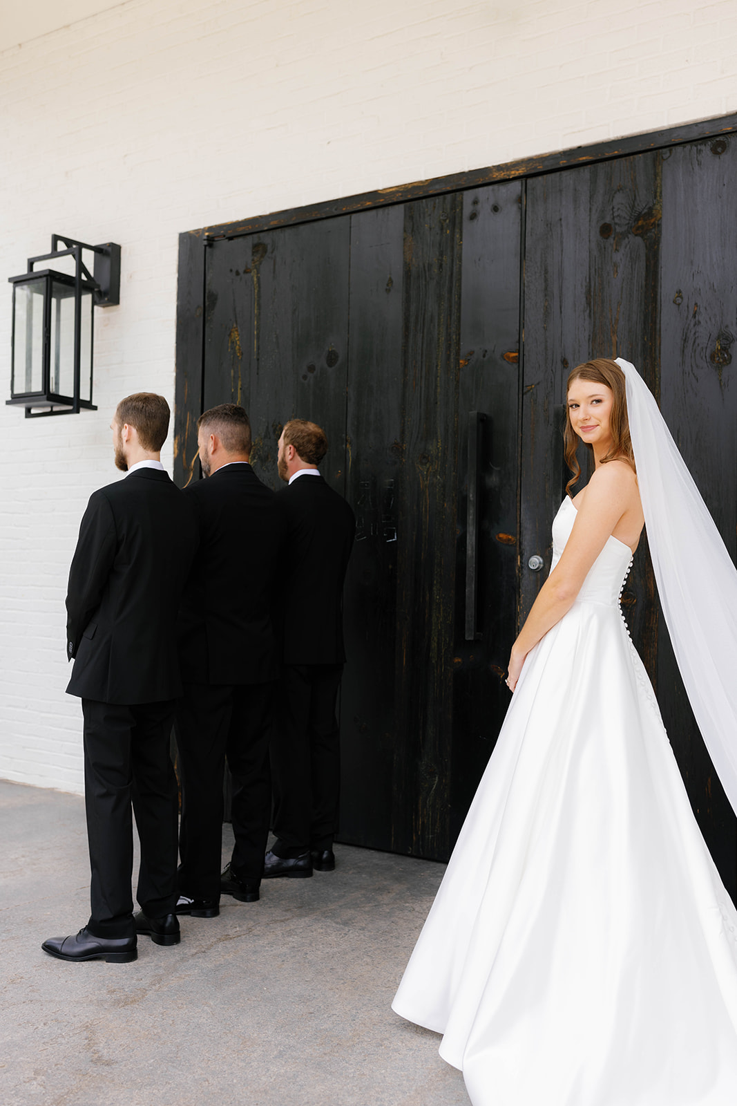 A smiling bride stands behind the groomsmen, ready for a first look reveal at her wedding at The 405.