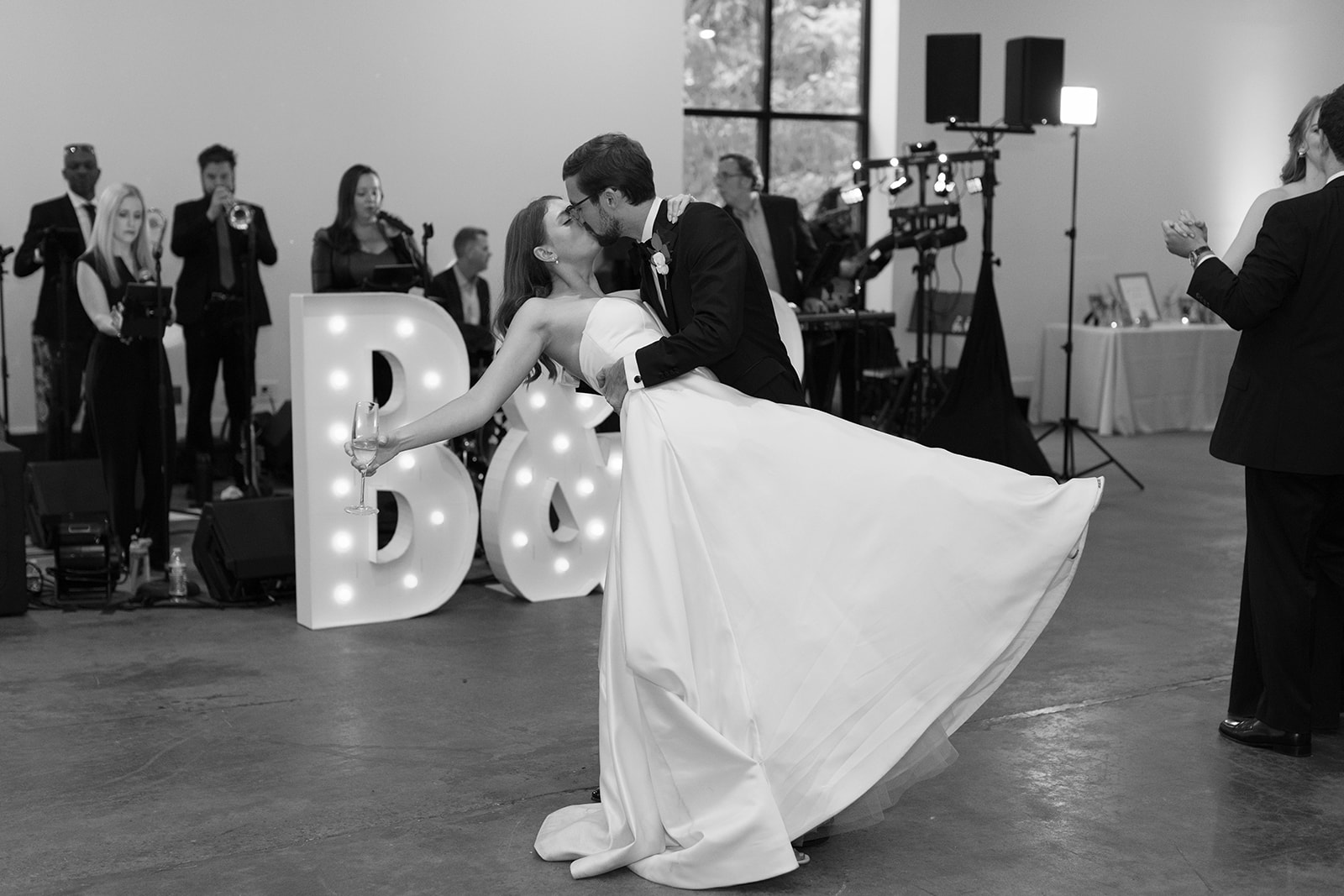 Groom dips the bride for a romantic kiss during their final dance under marquee initials.