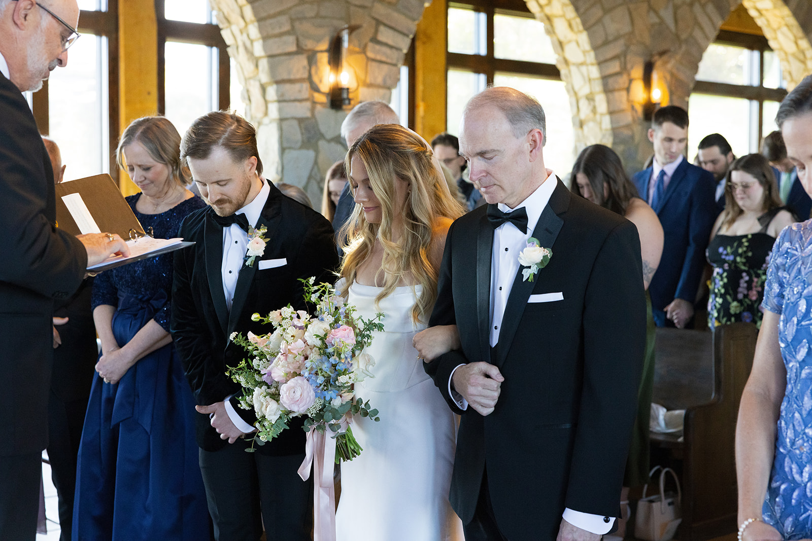 bride, groom, and guests bow their heads in prayer during their ceremony