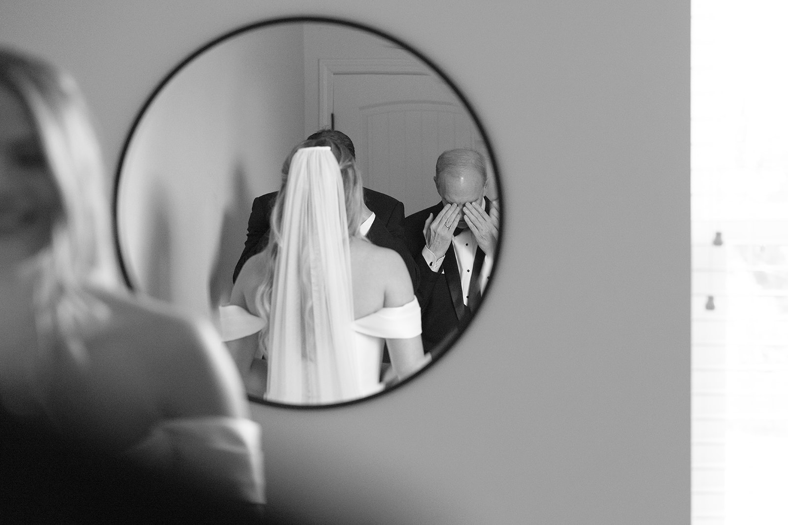 bride looks in mirror as father and brother cover their eyes for a first look