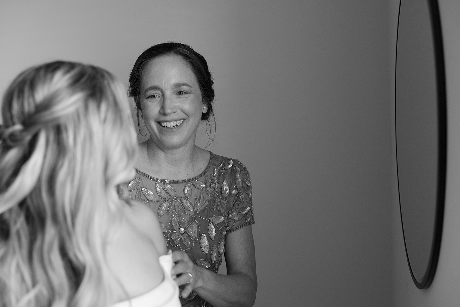 mother of the bride smiling as she watches her get ready