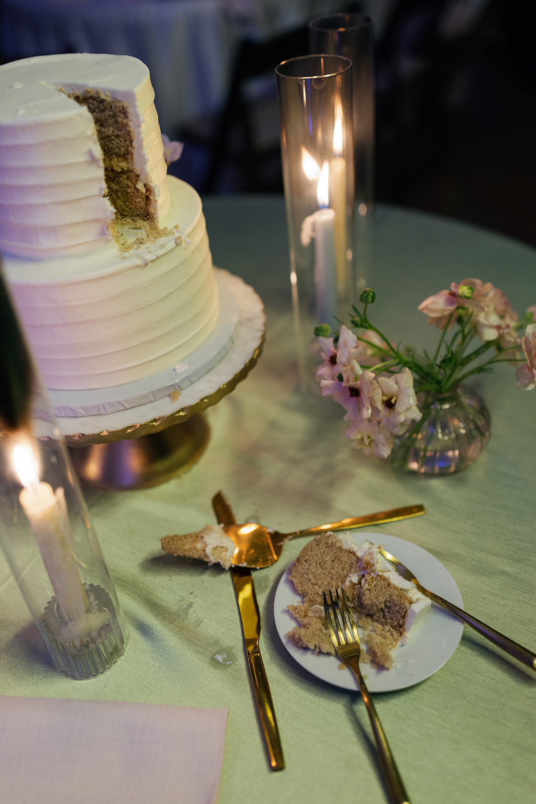 Candlelit table with floral centerpieces and a freshly cut cake at a timeless wedding 
