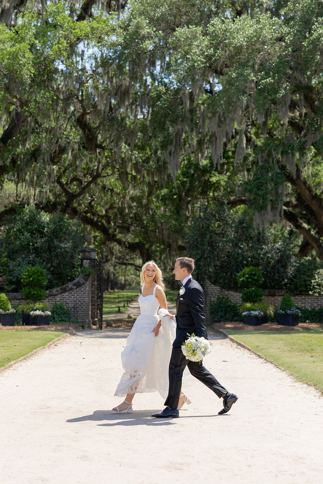 bride and groom walk in front of brick wall at Boone hall plantation