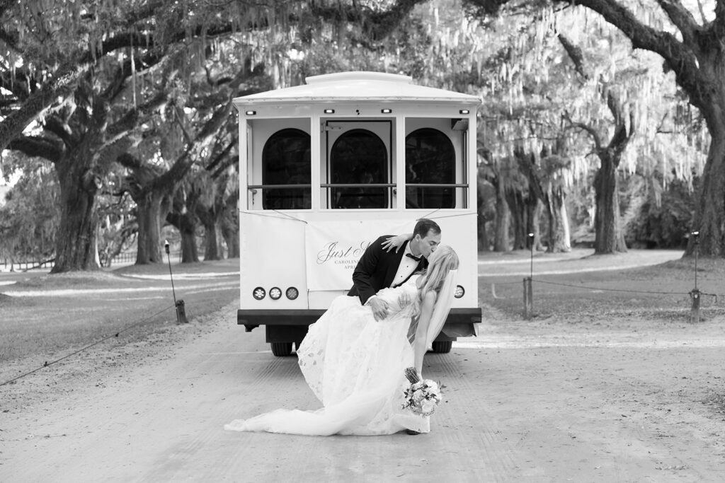 Bride and groom share a kiss in front of a trolley under the Avenue of Oaks