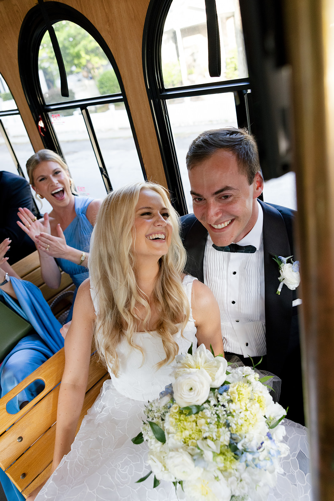 bride and groom laugh with their bridal party on the trolley ride to their wedding reception