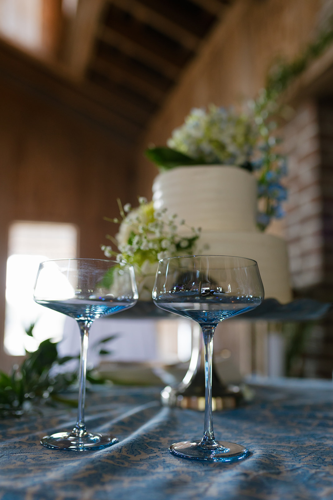 Close-up of blue-rimmed champagne glasses and a floral wedding cake at a Boone Hall Plantation wedding reception in Charleston, SC.