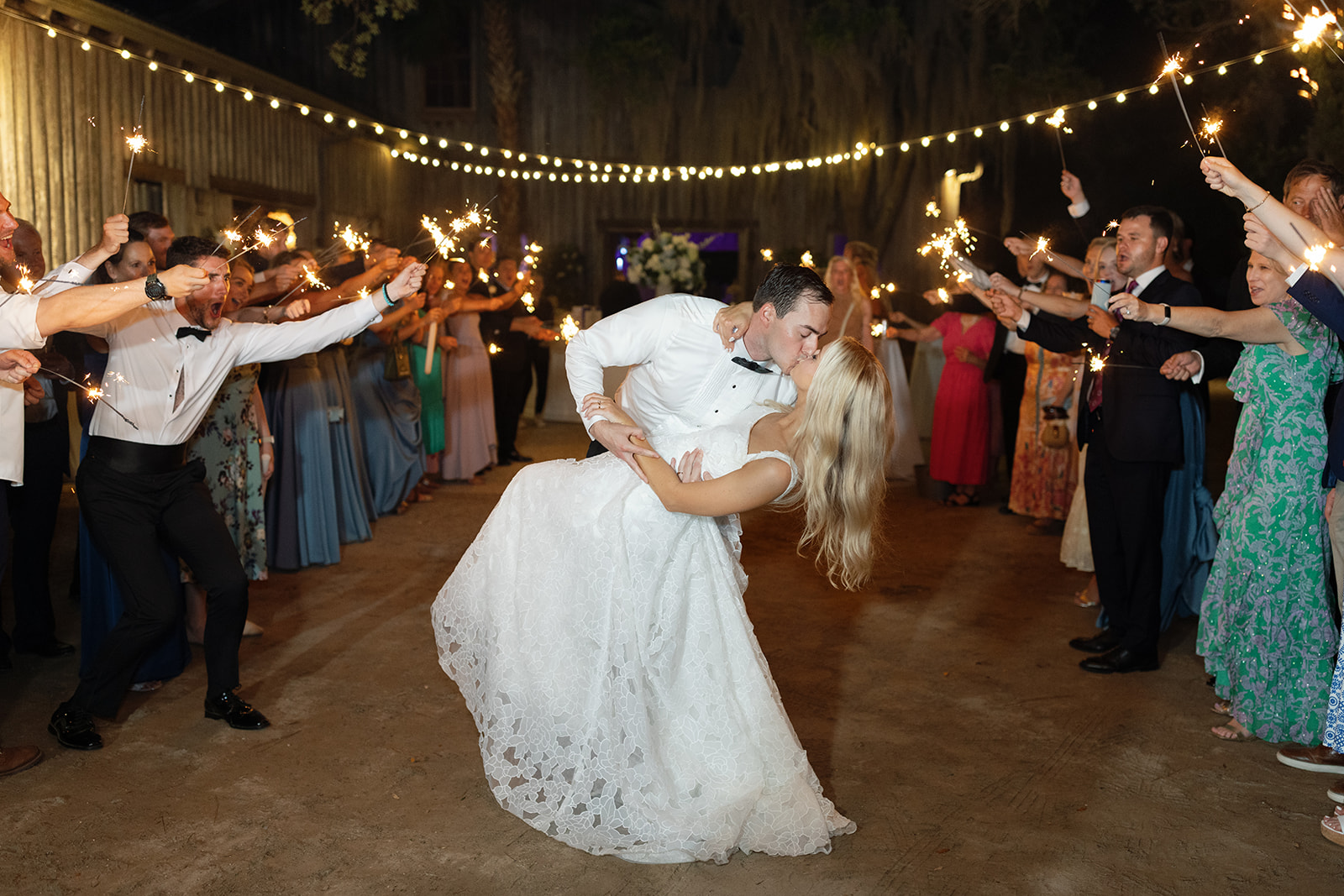 bride and groom kiss beneath a guest tunnel with sparklers at their wedding sendoff