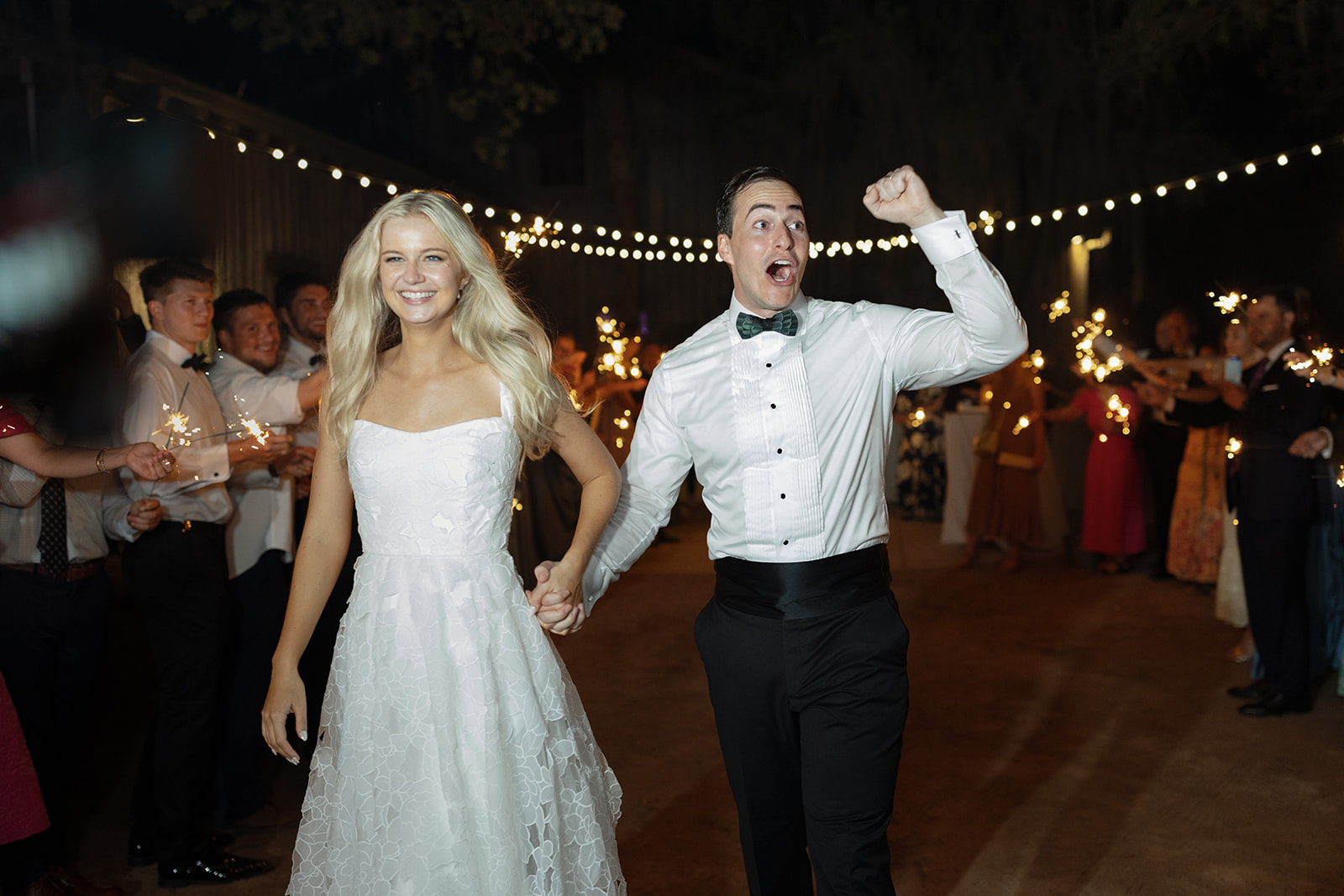 bride and groom walk through the guest tunnel with sparklers at their wedding sendoff as groom cheers