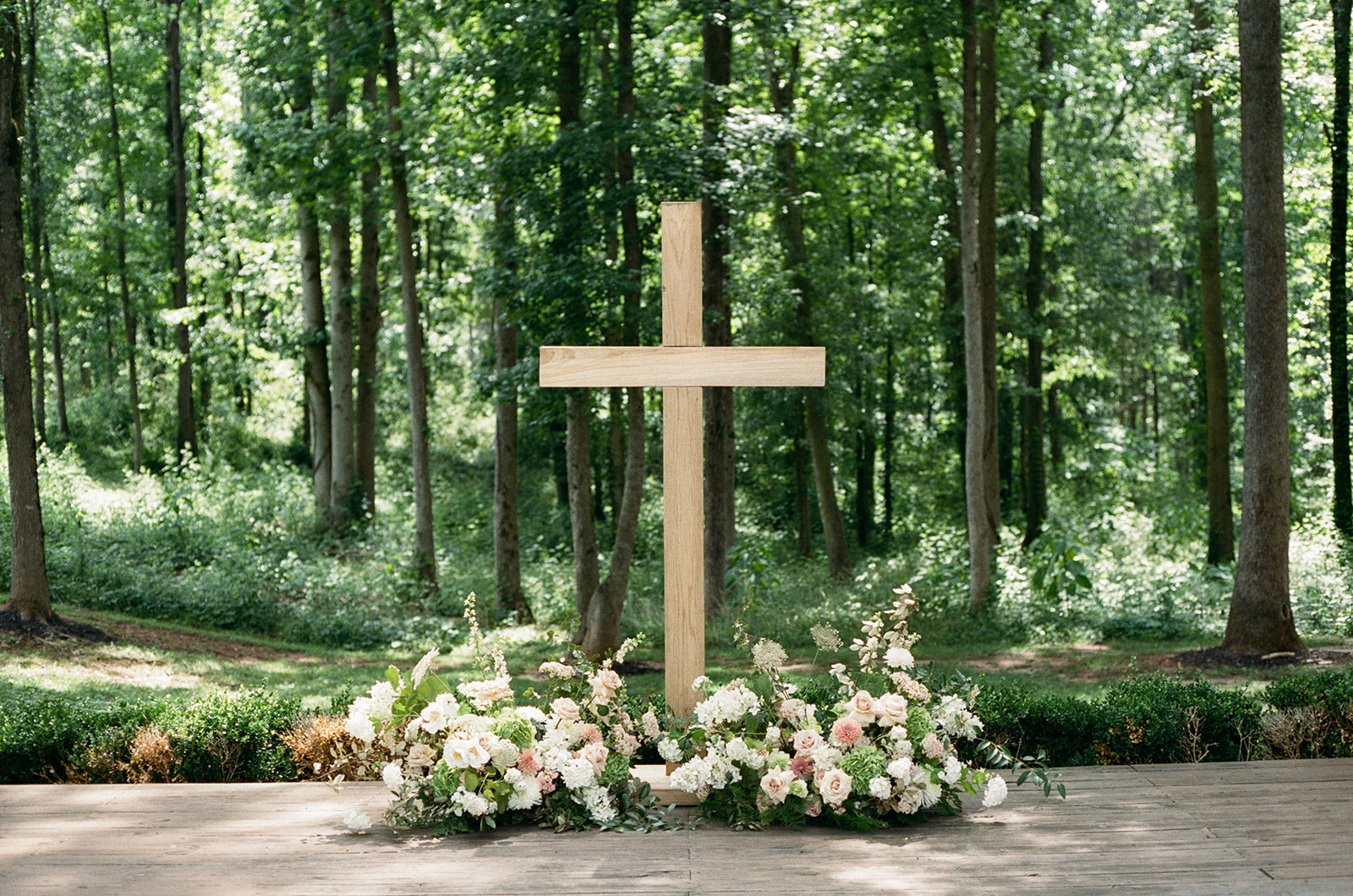 film photo of stunning pastel florals surrounding a large wooden cross at a South Carolina wedding ceremony 