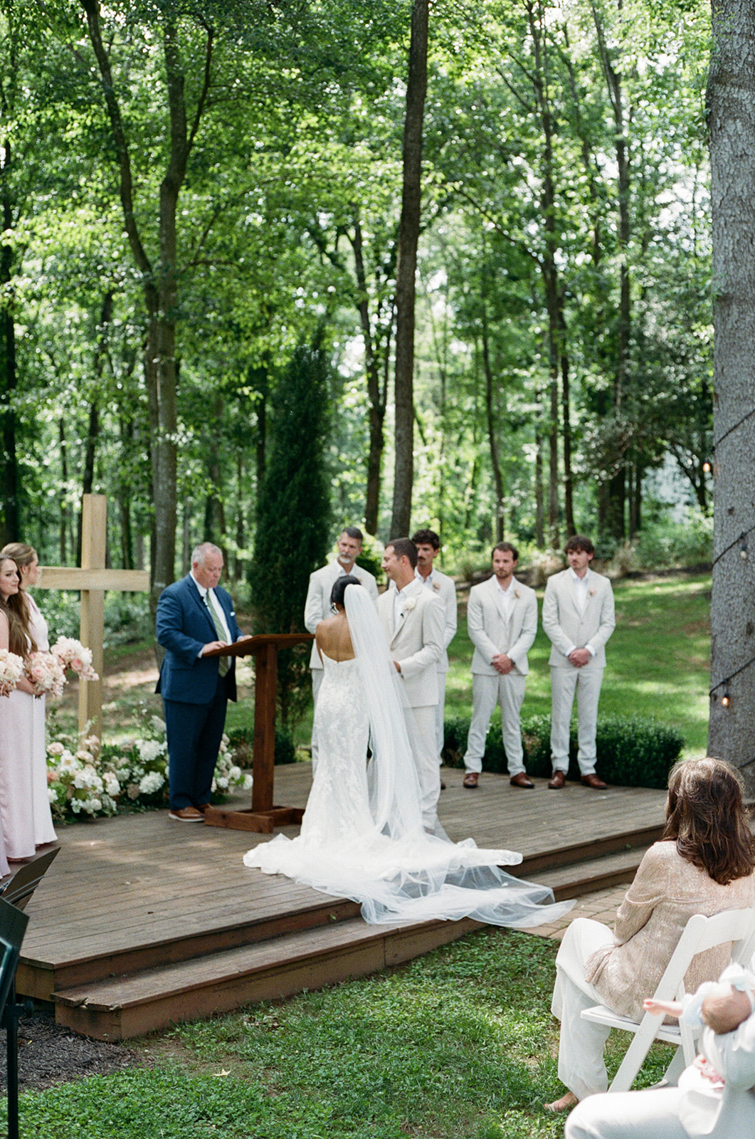 film photo of bride and groom exchanging vows among stunning pastel florals surrounding a large wooden cross at a South Carolina wedding ceremony 