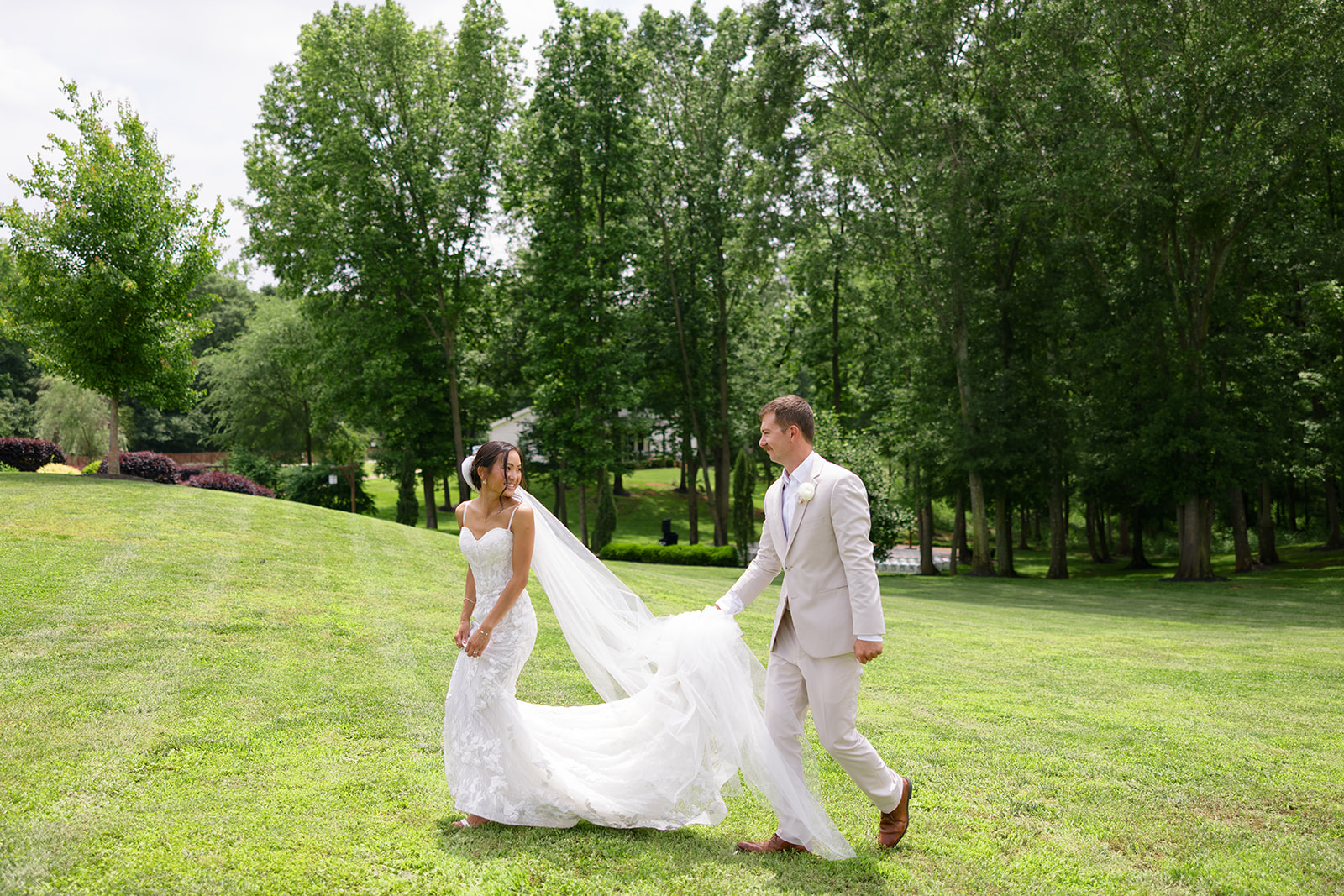 bride looks back smiling at the groom as they walk across the lawn
