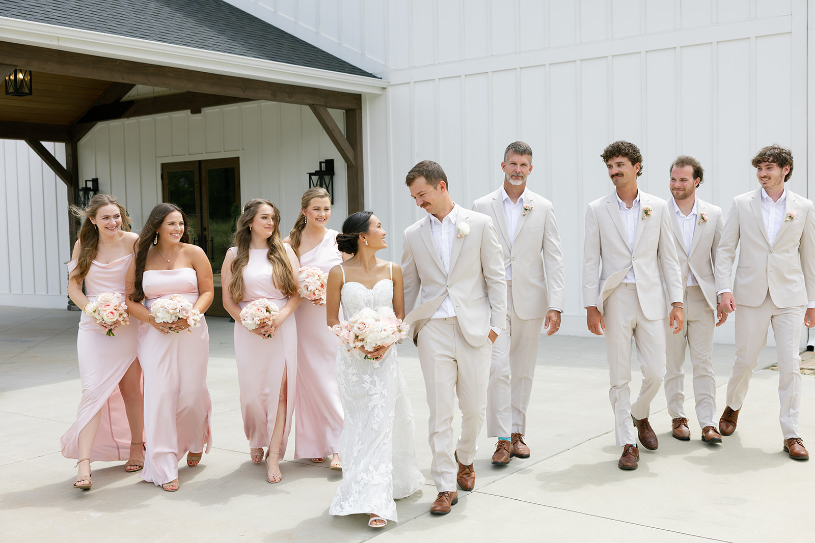 The bride and groom smile at each other as their bridal party walks behind them
