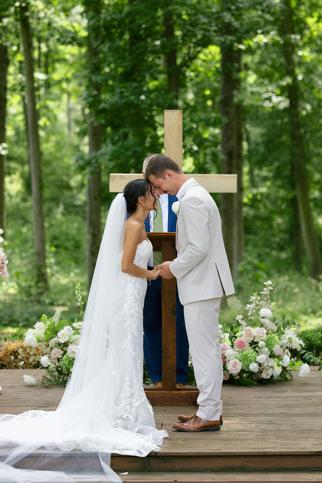 bride and groom share a moment in prayer after exchanging their wedding vows in front of a large wooden cross surrounded by florals