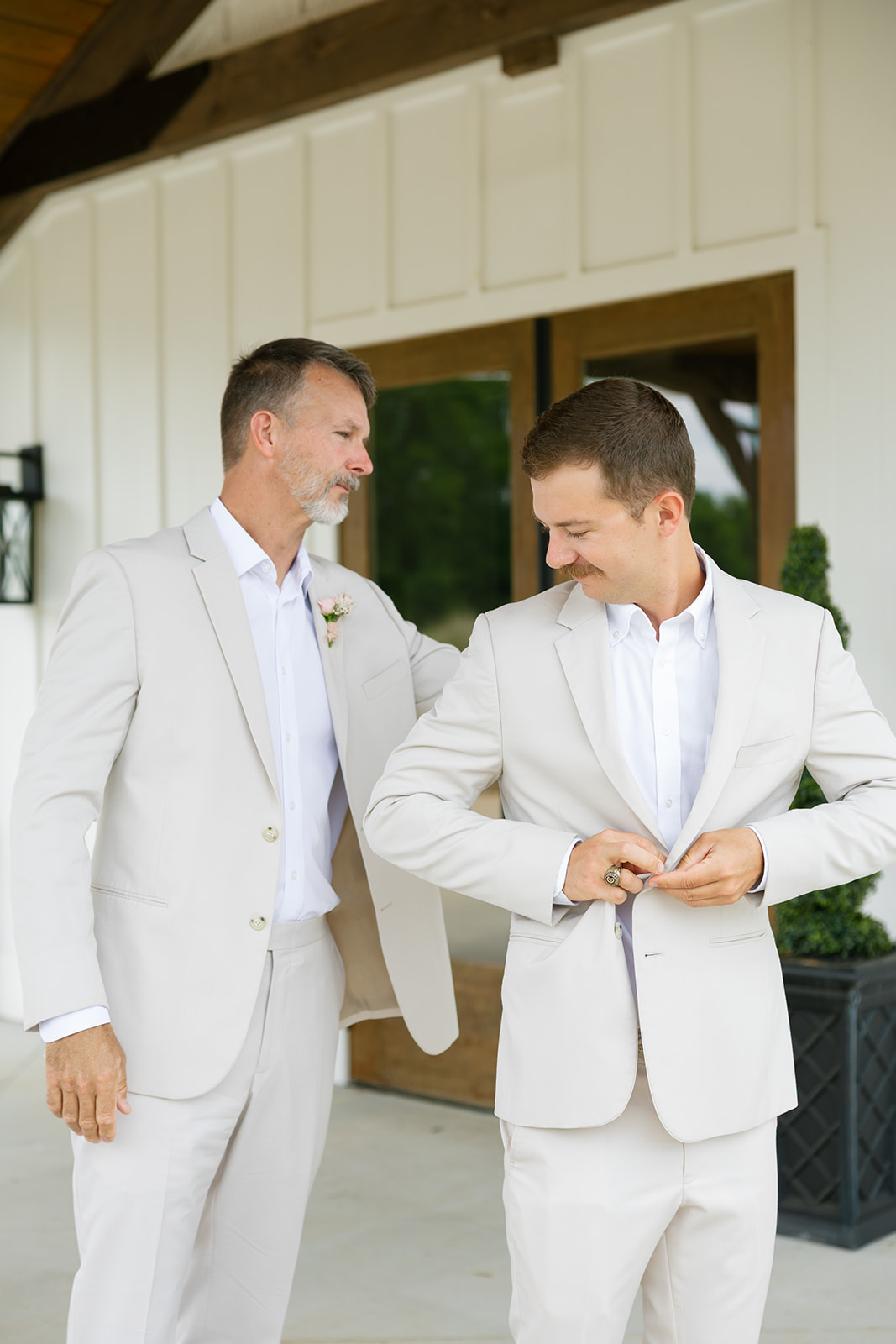 The father of the groom helps smooth out the groom's suit as they get ready
