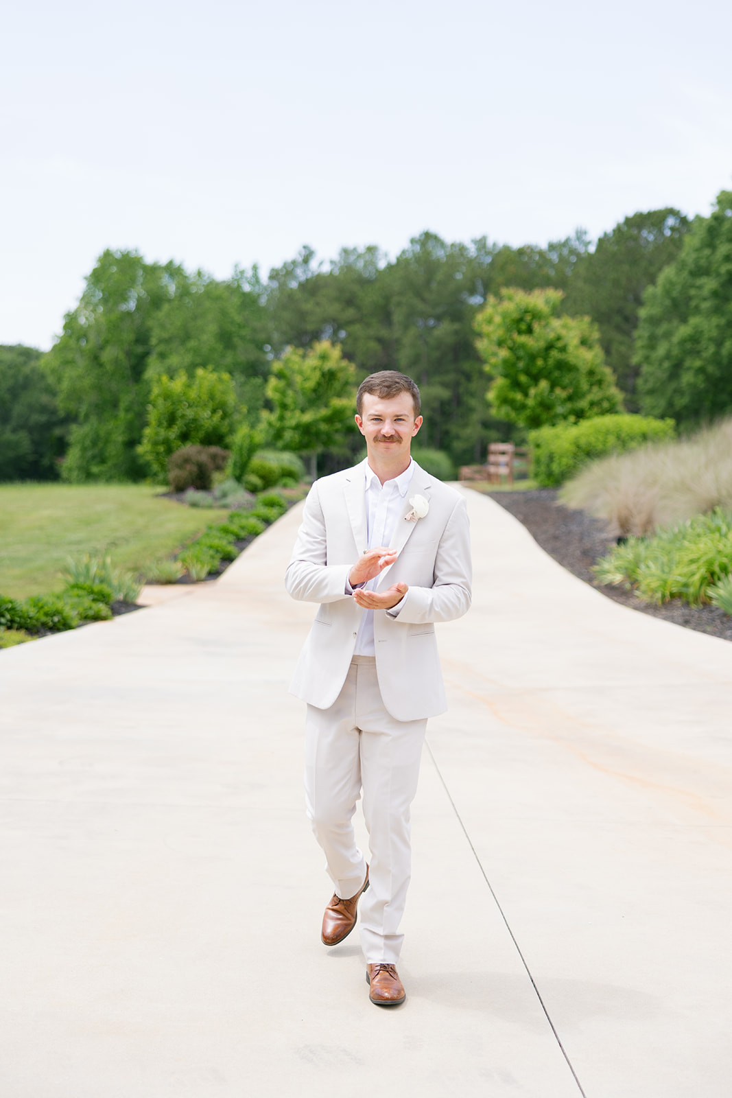 The groom claps with excitement as he walks down the path on the way to their wedding ceremony