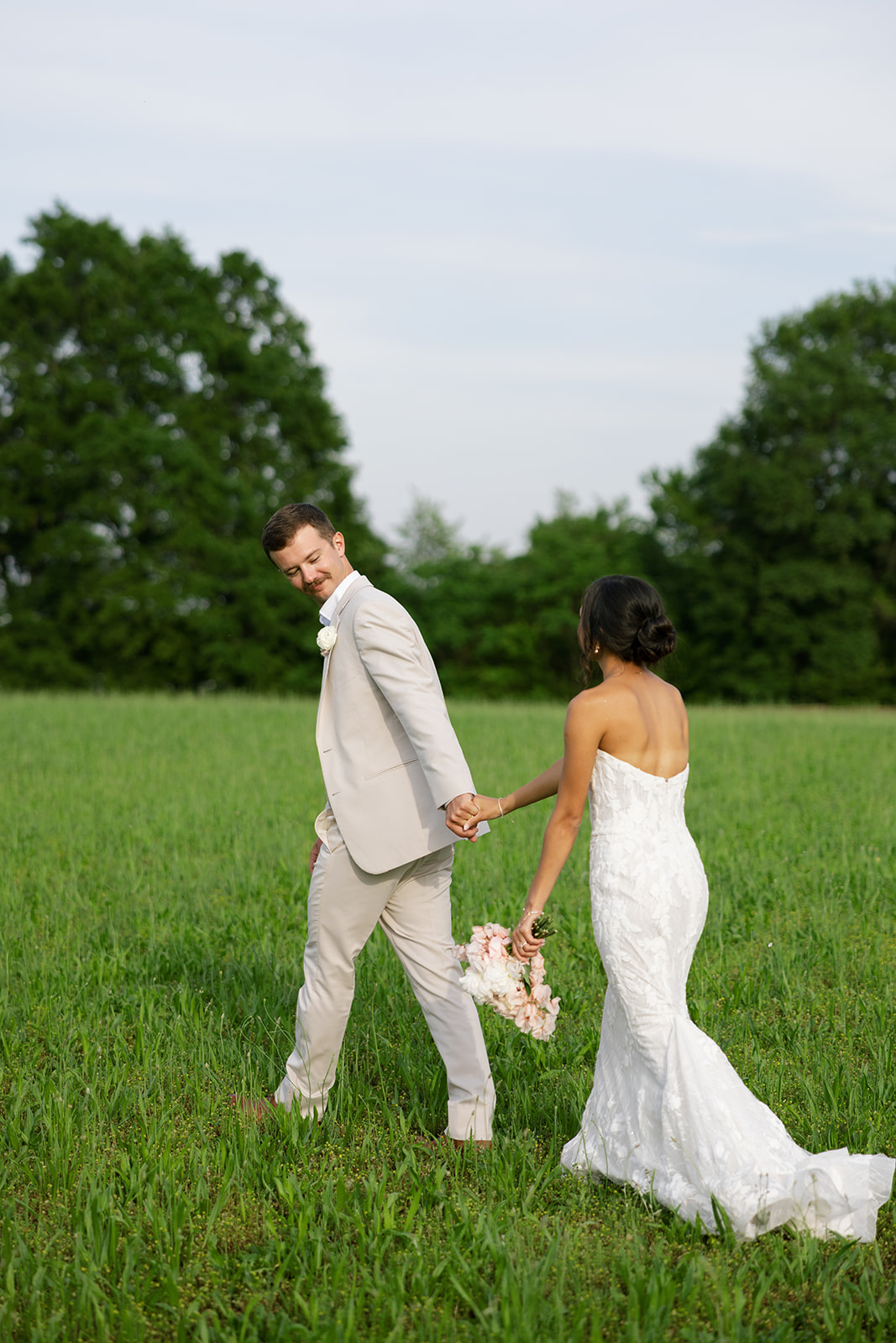 Groom looks back with a smile as he walks in front of his new wife through a field at their South Carolina wedding venue
