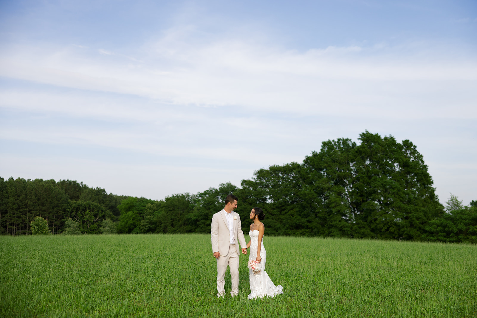 Bride and groom hold hands, sharing a smile in a field at their South Carolina wedding