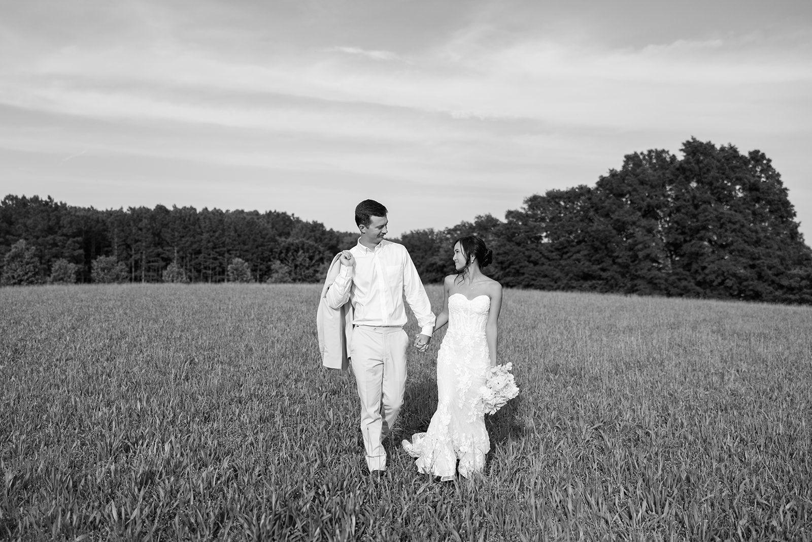 Newlyweds walking hand in hand through a field at their South Carolina wedding venue