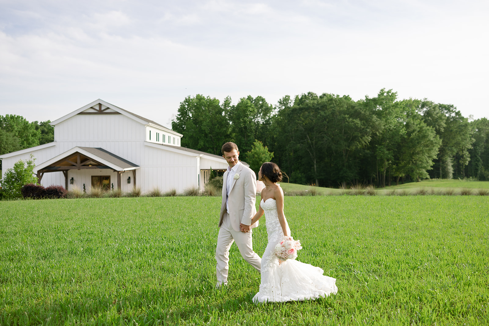 Groom walks with his new wife in the field outside The Venue at Edgewood