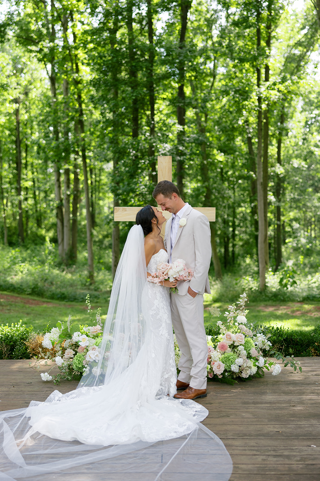 Newlyweds share a sweet moment in front of a large wooden cross surrounded by florals at their South Carolina wedding