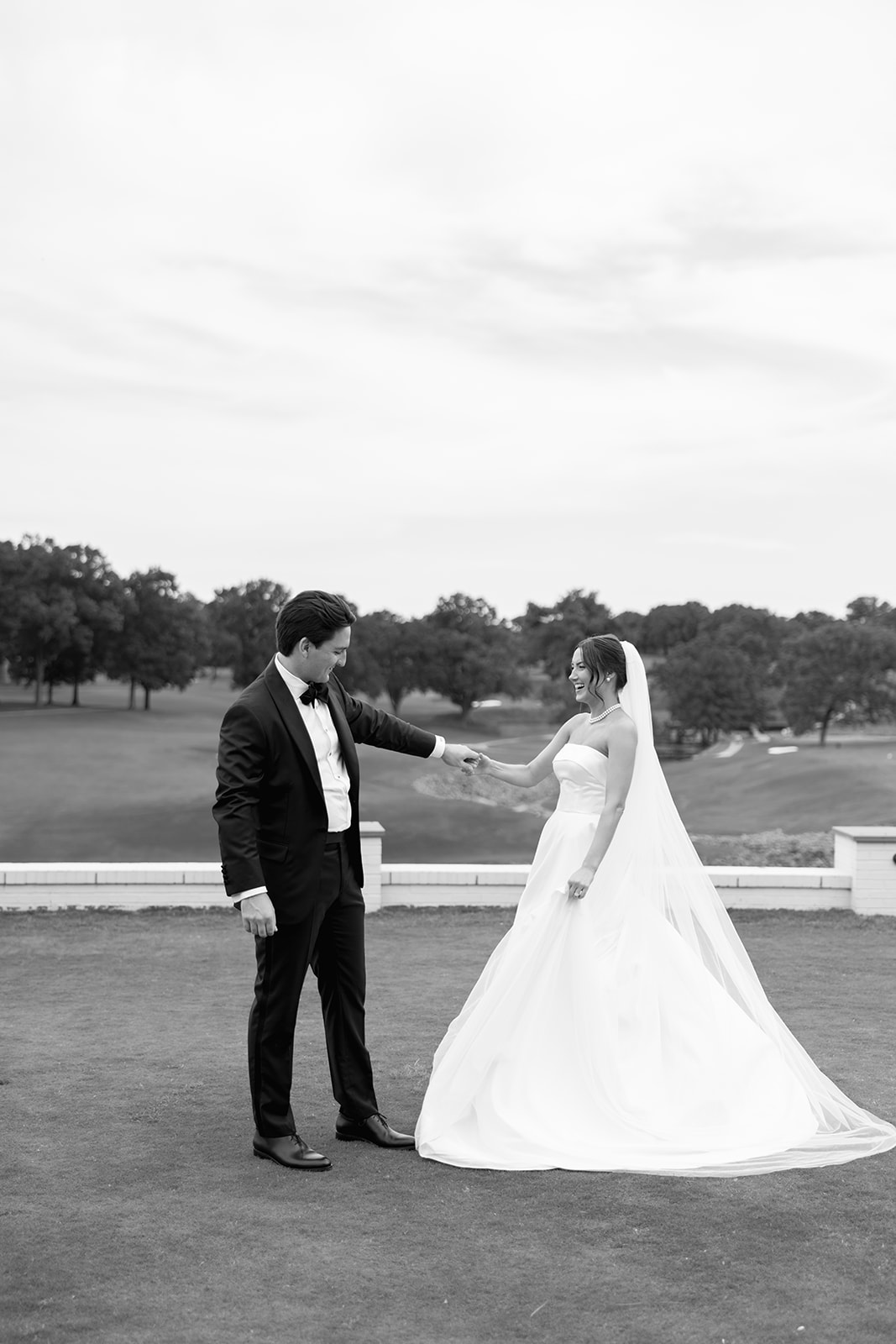 Black-and-white photo of groom twirling bride on a golf course, her veil flowing behind her.